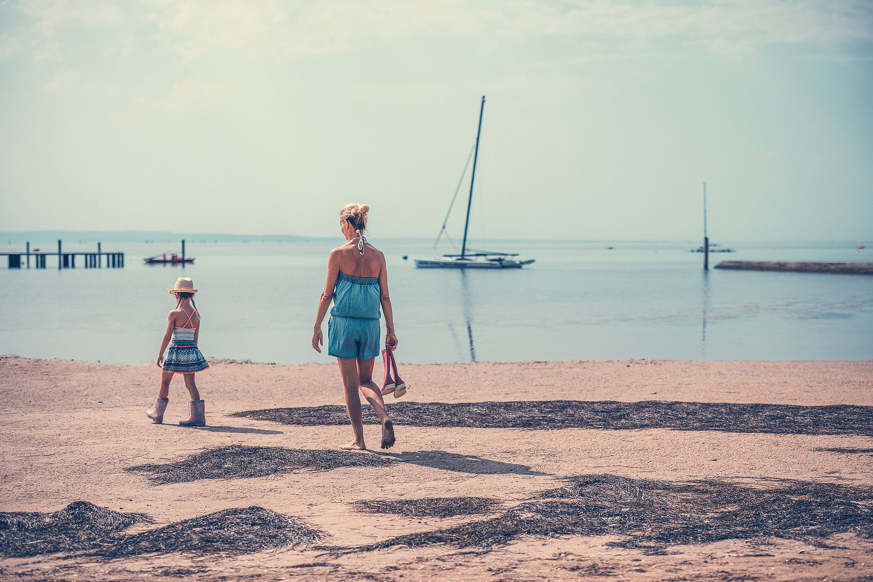 Mutter und Tochter am Strand mit Segelboot im Hintergrund